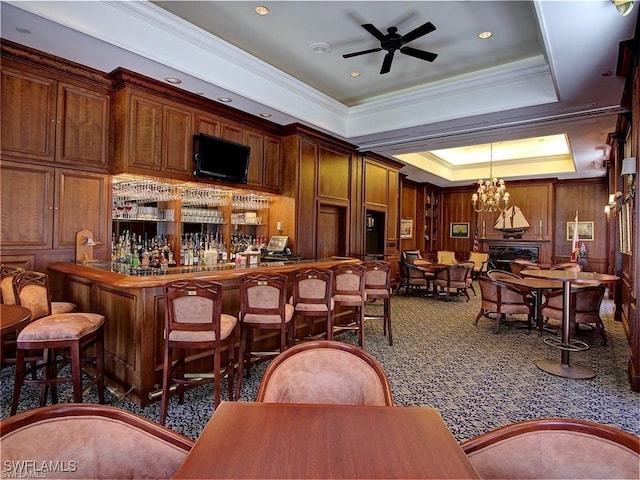 bar with ceiling fan with notable chandelier, decorative light fixtures, dark carpet, a raised ceiling, and crown molding