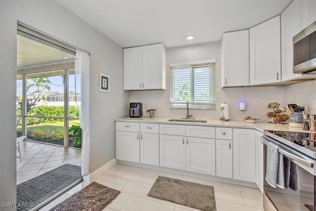 kitchen featuring sink, light tile patterned floors, appliances with stainless steel finishes, white cabinetry, and decorative backsplash