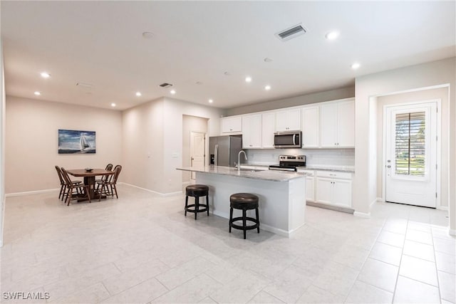 kitchen featuring sink, a breakfast bar, appliances with stainless steel finishes, white cabinets, and a center island with sink