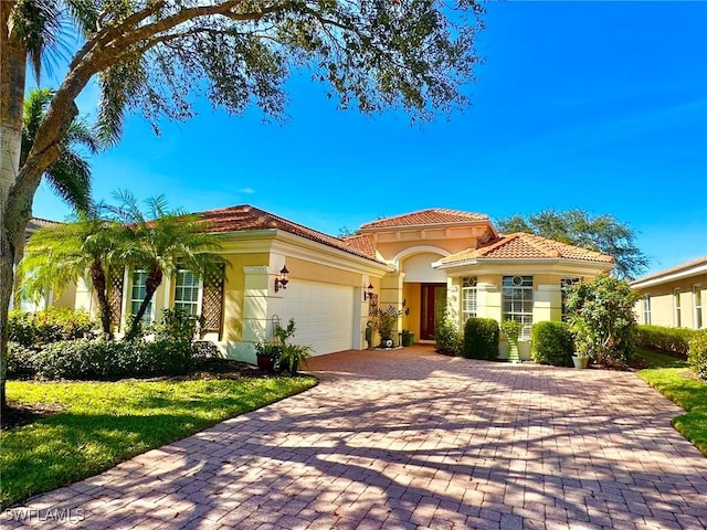 mediterranean / spanish home featuring a garage, a tiled roof, decorative driveway, and stucco siding