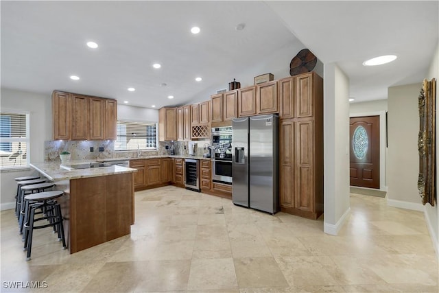 kitchen featuring a breakfast bar area, stainless steel fridge, kitchen peninsula, beverage cooler, and light stone countertops