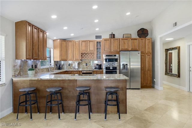 kitchen featuring lofted ceiling, appliances with stainless steel finishes, a kitchen breakfast bar, kitchen peninsula, and decorative backsplash