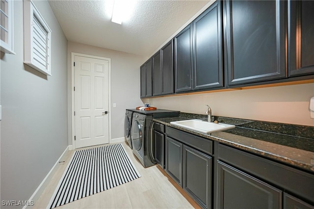 laundry room featuring cabinet space, a sink, a textured ceiling, washer and dryer, and baseboards