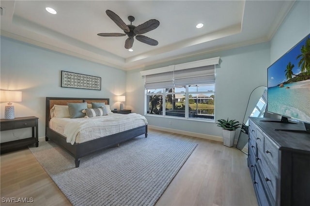 bedroom with ceiling fan, ornamental molding, light wood-type flooring, and a tray ceiling