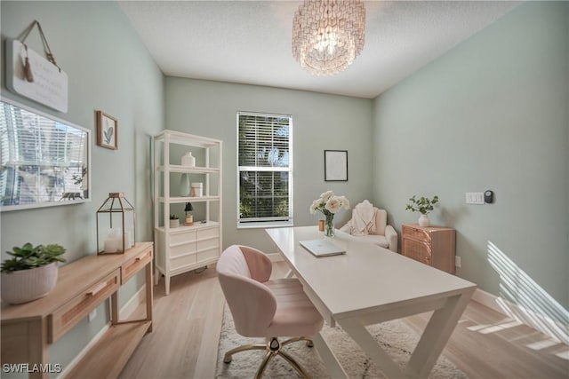 office area with a textured ceiling, light wood finished floors, baseboards, and an inviting chandelier