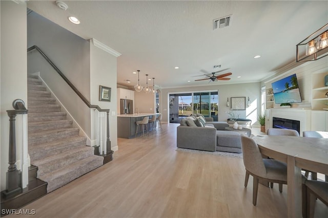 living room with ornamental molding, ceiling fan, and light wood-type flooring