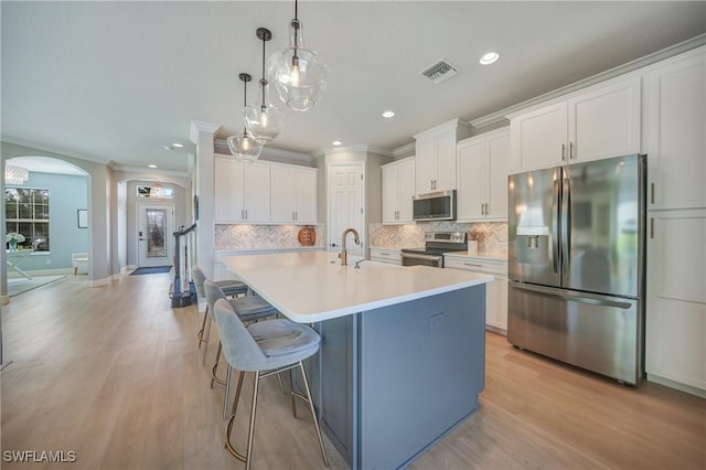 kitchen featuring appliances with stainless steel finishes, white cabinetry, a kitchen bar, hanging light fixtures, and a center island with sink