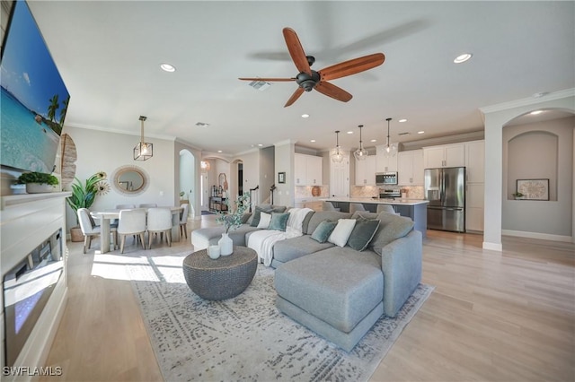 living area with light wood-style flooring, arched walkways, a ceiling fan, and ornamental molding