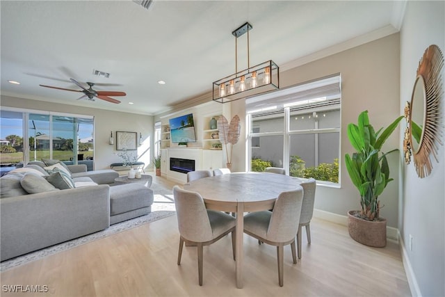 dining space with baseboards, visible vents, a glass covered fireplace, ornamental molding, and light wood-style floors