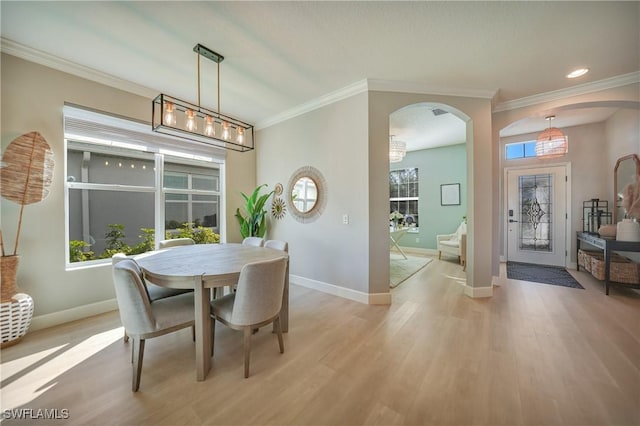 dining room with ornamental molding, arched walkways, light wood-style flooring, and baseboards