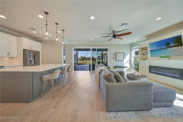 living room with crown molding, ceiling fan, light wood-type flooring, and built in shelves