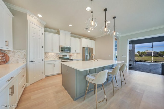 kitchen with a breakfast bar, hanging light fixtures, an island with sink, stainless steel appliances, and white cabinets