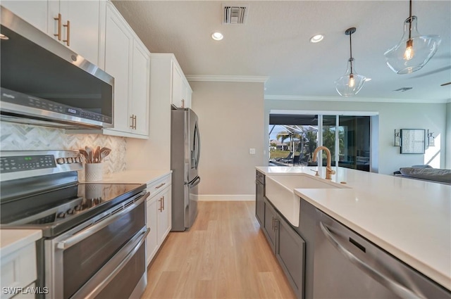 kitchen featuring sink, white cabinets, hanging light fixtures, stainless steel appliances, and crown molding