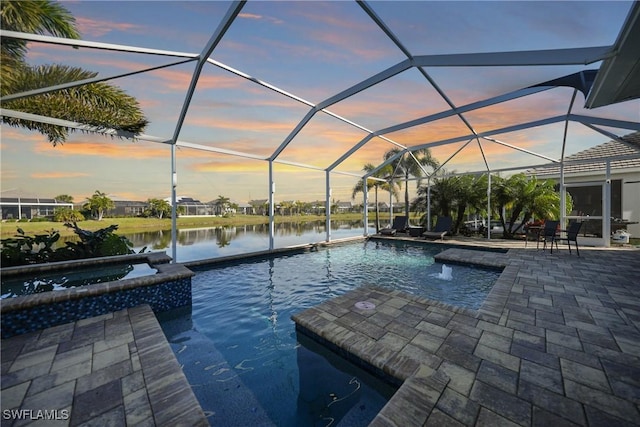 pool at dusk featuring a patio area, a water view, a lanai, and a pool with connected hot tub