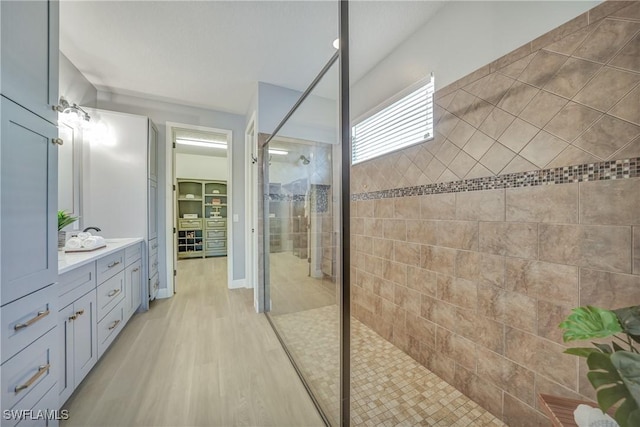 bathroom with a walk in shower, wood finished floors, a walk in closet, and vanity