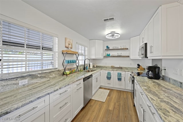 kitchen with sink, white cabinetry, light stone counters, light hardwood / wood-style flooring, and stainless steel appliances