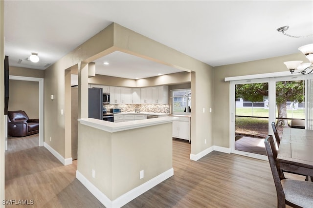 kitchen with appliances with stainless steel finishes, white cabinetry, backsplash, a chandelier, and light wood-type flooring