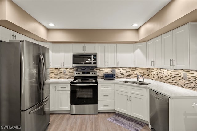 kitchen with stainless steel appliances, white cabinetry, sink, and light wood-type flooring