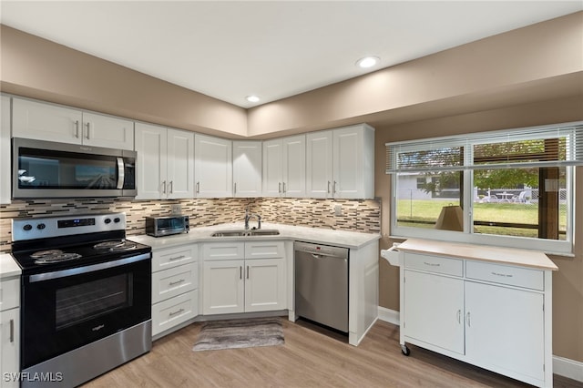 kitchen with sink, light wood-type flooring, white cabinets, stainless steel appliances, and backsplash