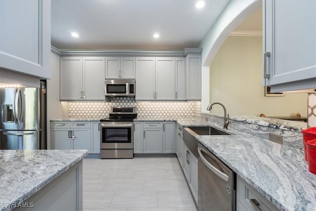 kitchen with gray cabinets, sink, backsplash, stainless steel appliances, and light stone countertops