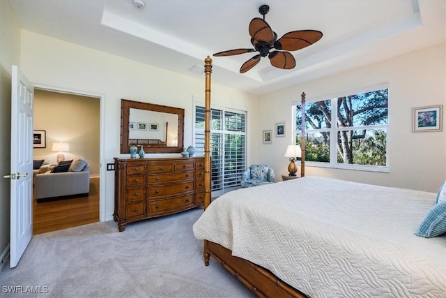 bedroom featuring light colored carpet, a raised ceiling, and ceiling fan