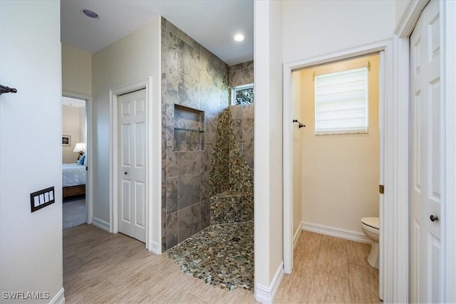 bathroom featuring toilet, hardwood / wood-style floors, and a tile shower