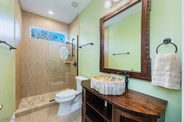 bathroom featuring vanity, a tile shower, and toilet