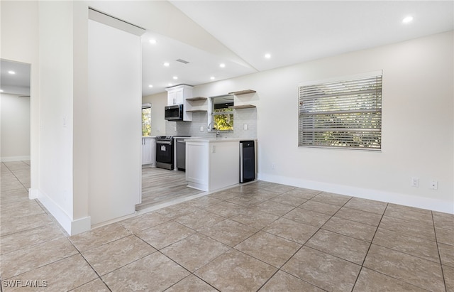 kitchen with white cabinetry, backsplash, vaulted ceiling, appliances with stainless steel finishes, and light tile patterned flooring