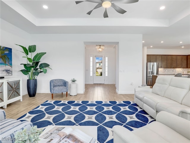 living room with a tray ceiling, ceiling fan with notable chandelier, and light wood-type flooring