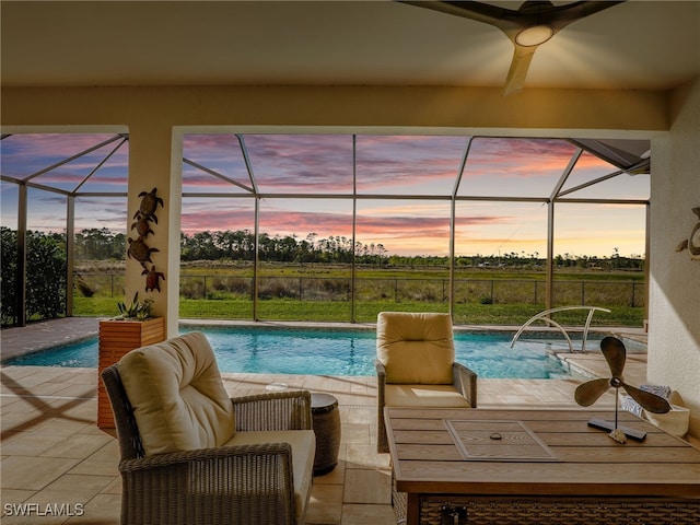 pool at dusk featuring pool water feature, ceiling fan, a lanai, and a patio area