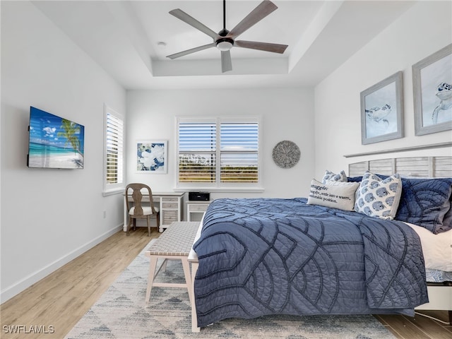 bedroom with a raised ceiling, ceiling fan, and light wood-type flooring