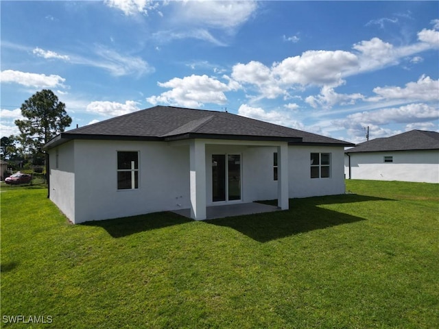 rear view of house with roof with shingles, a lawn, and stucco siding