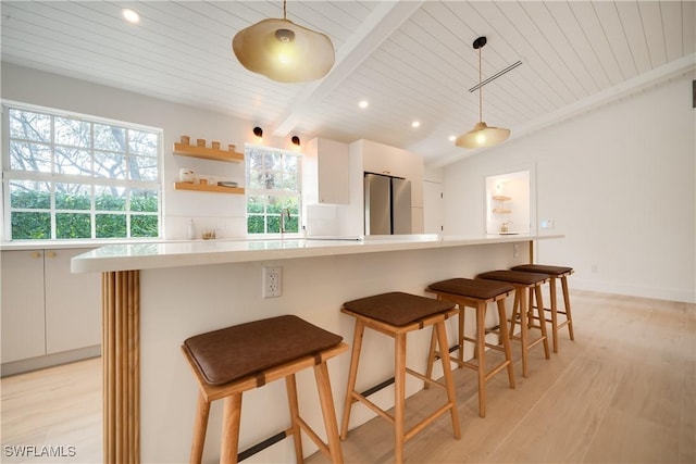 kitchen featuring white cabinets, freestanding refrigerator, vaulted ceiling with beams, light countertops, and light wood-style floors