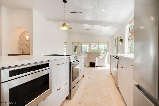 kitchen with pendant lighting, light countertops, lofted ceiling with beams, appliances with stainless steel finishes, and white cabinetry