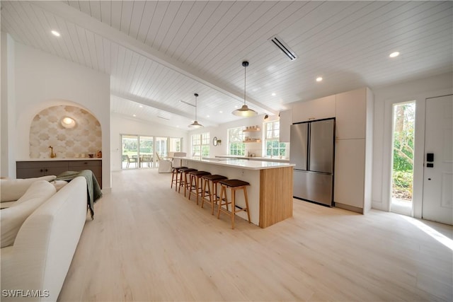 kitchen featuring vaulted ceiling with beams, a breakfast bar, open floor plan, light wood-type flooring, and freestanding refrigerator