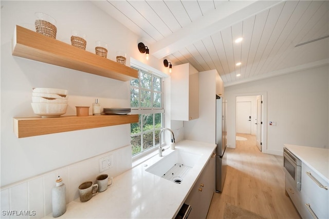 kitchen with open shelves, light countertops, lofted ceiling with beams, appliances with stainless steel finishes, and a sink