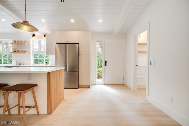 kitchen with light countertops, beam ceiling, light wood-style flooring, and freestanding refrigerator