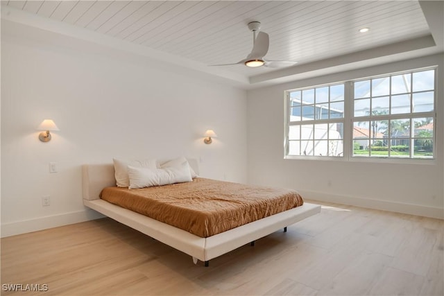 bedroom featuring wooden ceiling, light wood-style floors, baseboards, and a tray ceiling