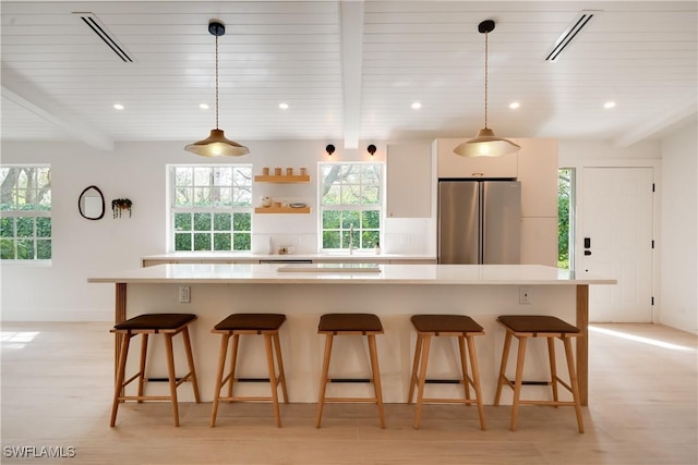 kitchen with beamed ceiling, a center island, freestanding refrigerator, and light countertops