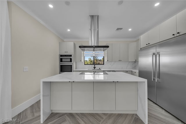 kitchen featuring a kitchen island, appliances with stainless steel finishes, white cabinetry, light stone counters, and crown molding