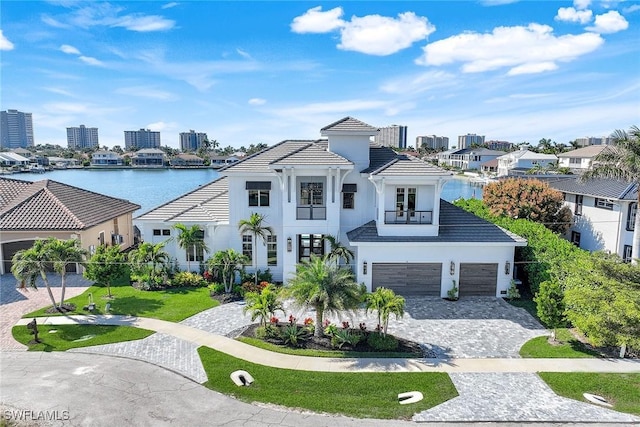 view of front of property featuring a garage, a front lawn, a balcony, and a water view