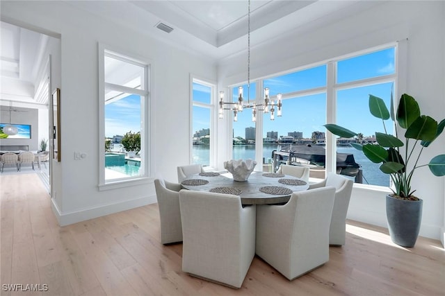 dining space with a water view, a chandelier, light wood-type flooring, and a tray ceiling