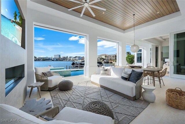 interior space with wood ceiling, ceiling fan, a water view, a tray ceiling, and a fireplace