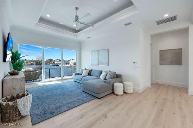 living room featuring a water view, ceiling fan, a raised ceiling, and light wood-type flooring