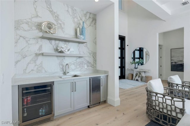 bar featuring tasteful backsplash, sink, beverage cooler, and light hardwood / wood-style floors