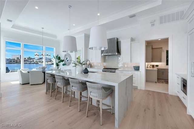 kitchen with pendant lighting, white cabinetry, wall chimney exhaust hood, a water view, and a spacious island