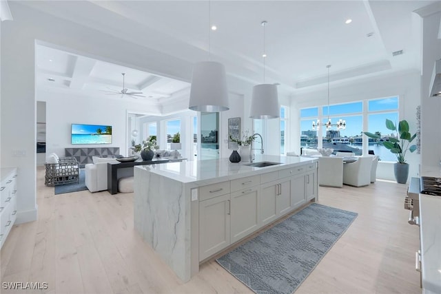 kitchen with sink, hanging light fixtures, a center island with sink, light stone countertops, and white cabinets