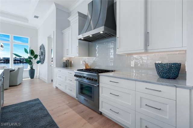 kitchen with extractor fan, high end range, light hardwood / wood-style flooring, light stone countertops, and white cabinets