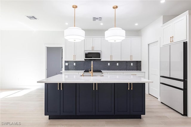 kitchen featuring decorative light fixtures, an island with sink, white cabinets, and refrigerator