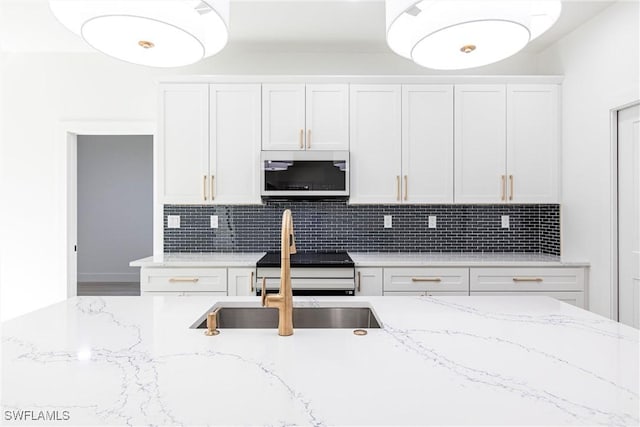 kitchen featuring light stone countertops, sink, decorative backsplash, and white cabinets